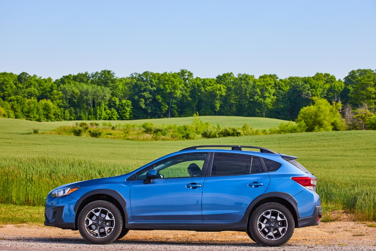 Side view of a blue Subaru Crosstrek small SUV with All Wheel Drive parked beside a green field.